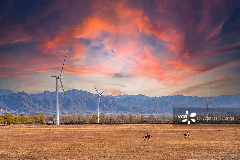 日落红云下的康西草原、奔跑的骏马、风力发电风车与群山图片素材