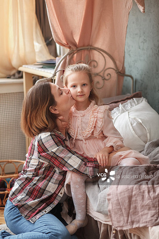 俄罗斯，母亲坐在家里的床上亲吻女儿图片素材