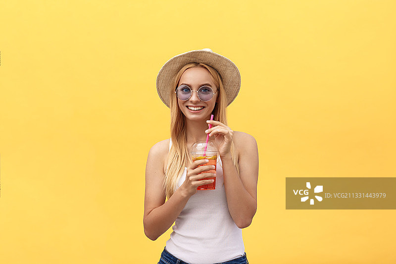 微笑的年轻女子的肖像拿着饮料，而站在黄色的背景图片素材