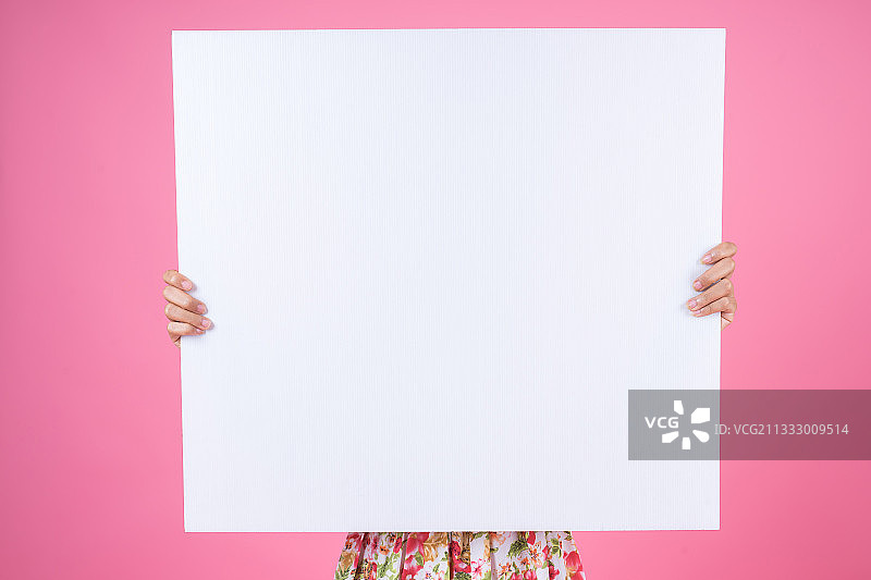 一个年轻女子在粉红色的背景下举着空白的海报图片素材