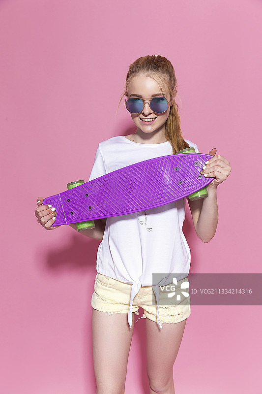 粉红色背景上放着滑板的快乐小女孩图片素材