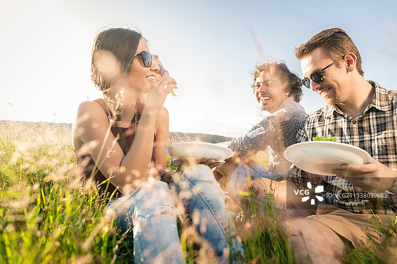 年轻人在夏天烧烤野餐，一起坐在草地上吃饭图片素材