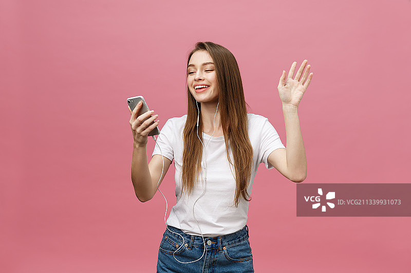 微笑的年轻女子用手机在粉红色的背景图片素材