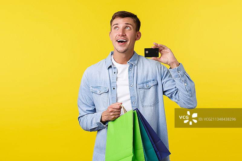 男子拿着购物袋和信用卡，背景为黄色图片素材
