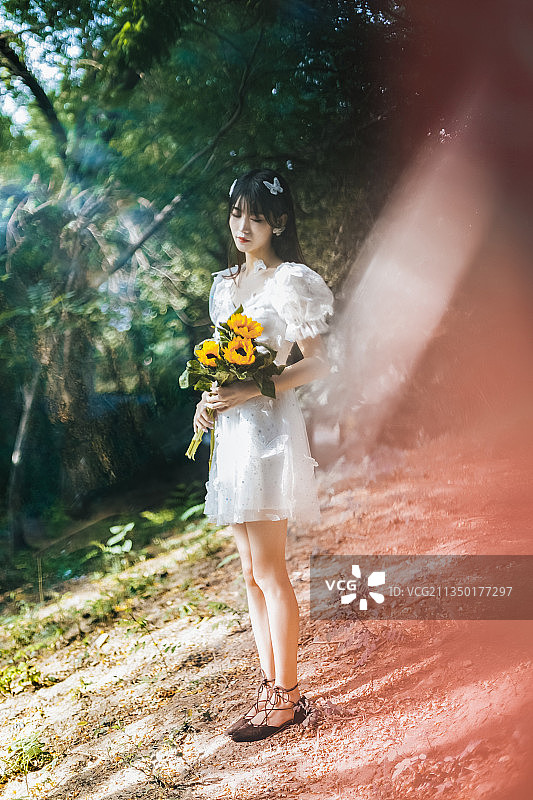 清晨树林里穿着白色连衣裙拿着花朵的女孩图片素材