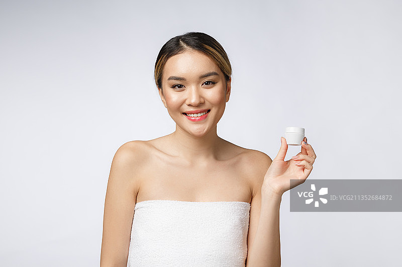 微笑的年轻女子的肖像手持保湿瓶在白色的背景图片素材