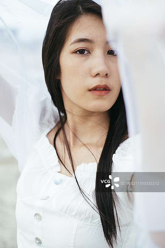 特写-时髦的年轻亚洲长黑发女人新娘与白色面纱的肖像。图片素材