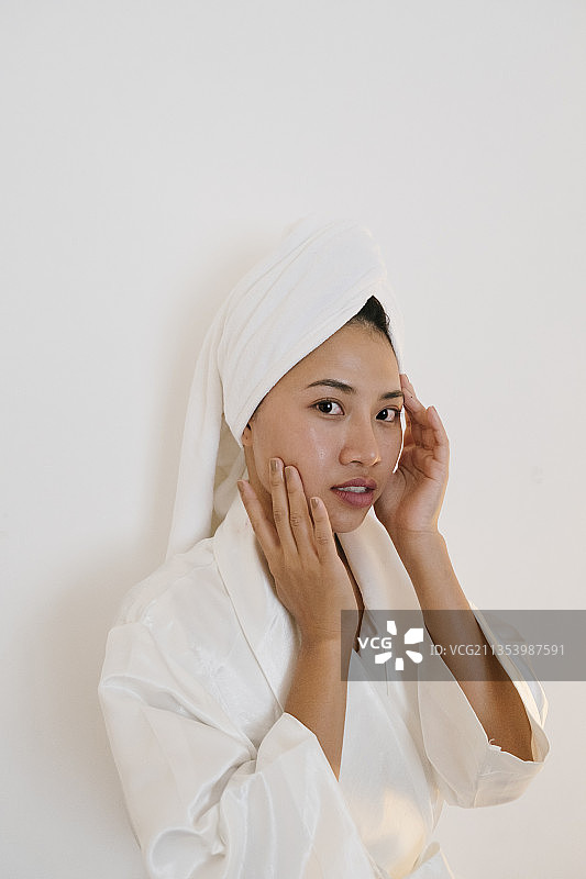 性感的亚洲泰国女人在白色浴袍应用护肤霜在她的脸孤立的白色背景。图片素材
