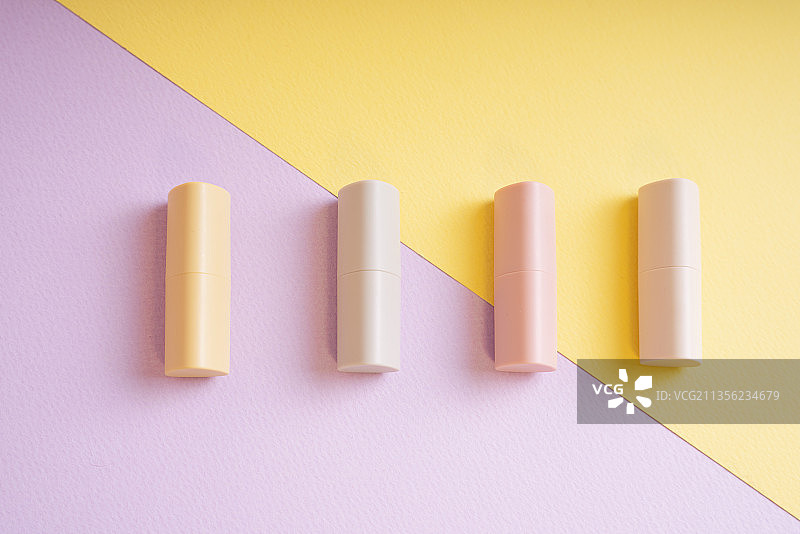 商业产品-一组柔和的米色唇膏在黄色和紫色背景。图片素材