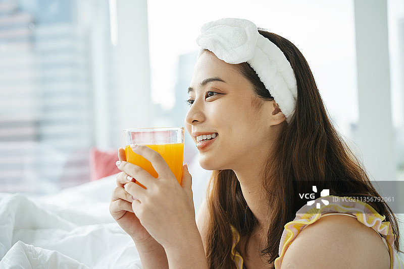 年轻的亚洲深色头发的女人戴着白色的头巾，手里拿着一杯橙汁。图片素材