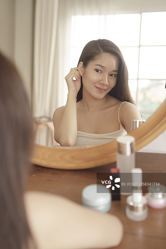 年轻的亚洲美女正对着镜子往脸上涂护肤霜。图片素材