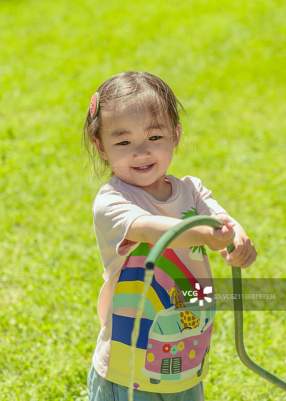 小女孩在别墅花园草坪上浇水降温图片素材