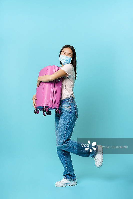 年轻女子拿着行李，站在蓝色背景下图片素材