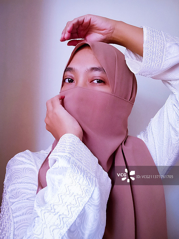 年轻女人的特写，用围巾遮住脸靠墙图片素材
