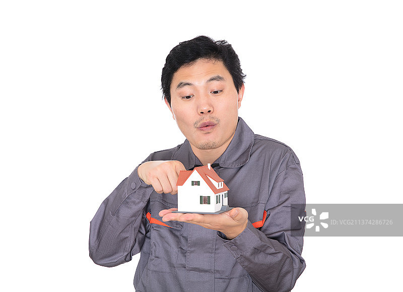 白背景前的建筑工人惊讶的用手指着另一只手里的房子模型图片素材