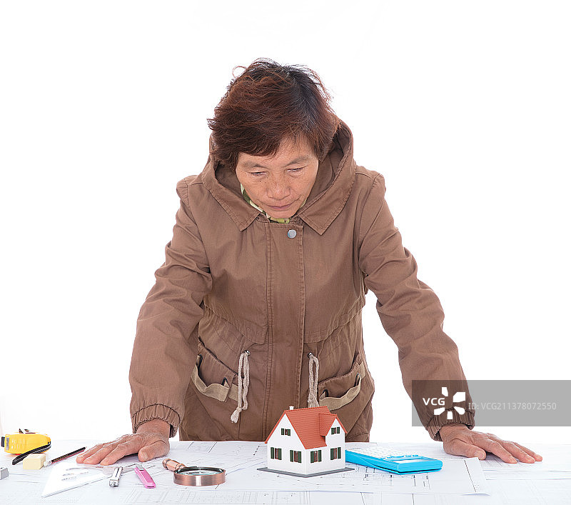 资深建筑设计师趴在桌子上对着图纸和房屋模型沉思图片素材