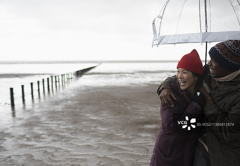 在潮湿的冬季海滩上，幸福的情侣在雨伞下拥抱图片素材