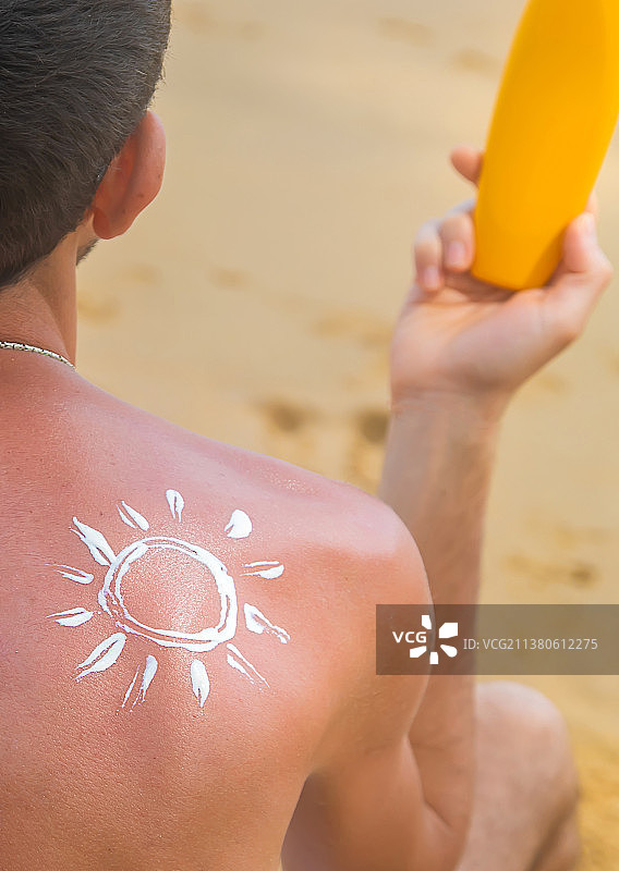 一个男人在沙滩上，背上涂着防晒霜选择性聚焦图片素材
