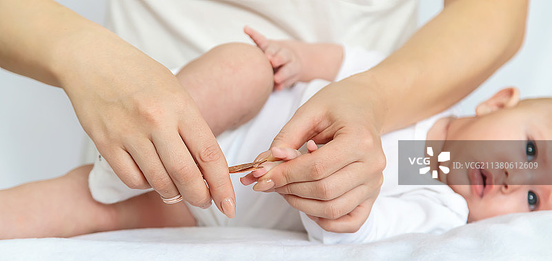 母亲在浅色背景下剪宝宝指甲选择性聚焦图片素材