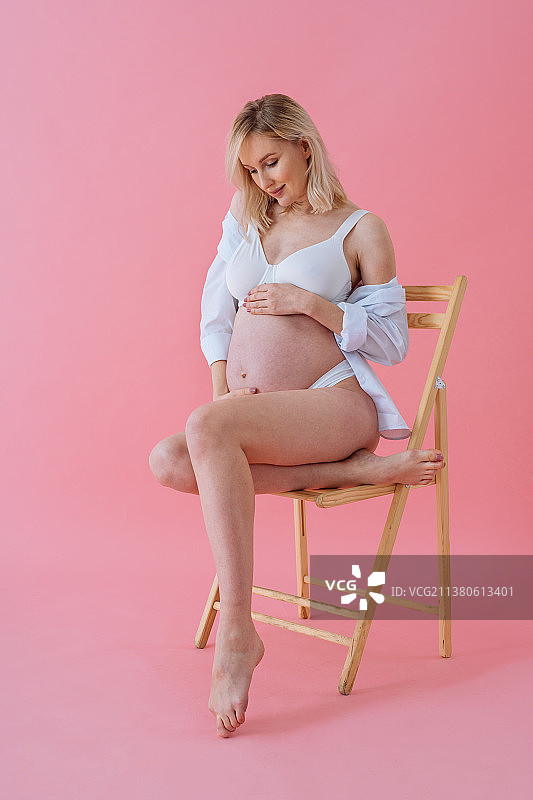 美丽的孕妇，母亲和怀孕的概念，肖像的孕妇坐在凳子上对粉红色的背景图片素材