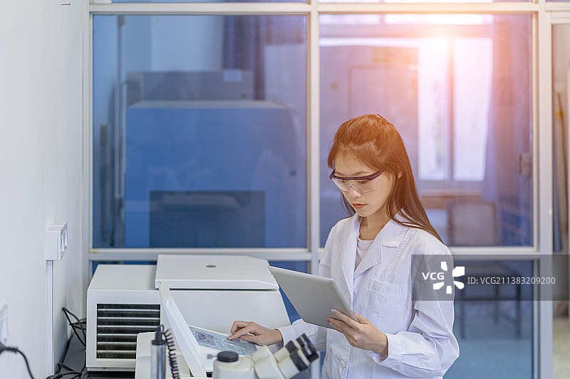 一身穿白大褂年青女子在实验室手拿平板电脑图片素材