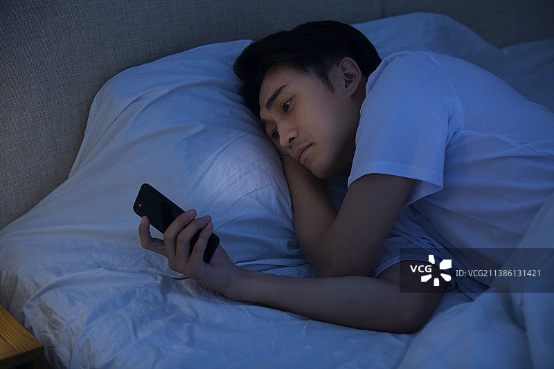 年轻男子深夜躺在床上玩手机图片素材