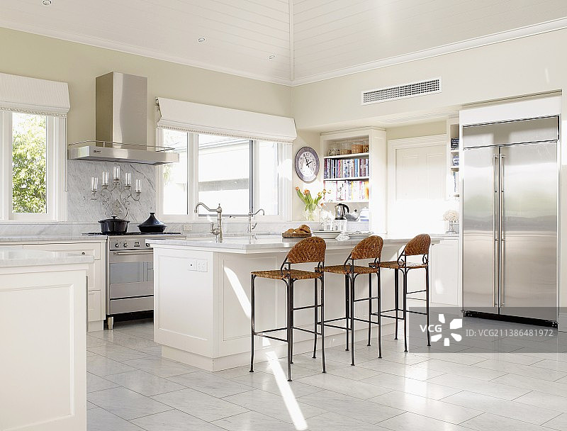 宽敞的白色厨房，有长长的厨房柜台，不锈钢门面和柜台高柳条凳图片素材