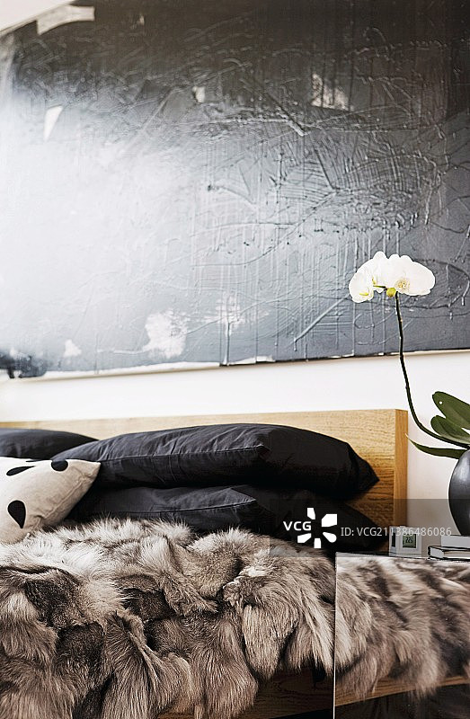黑色的枕头和毛皮毛毯堆叠在床上，下面是墙上的黑色绘画图片素材