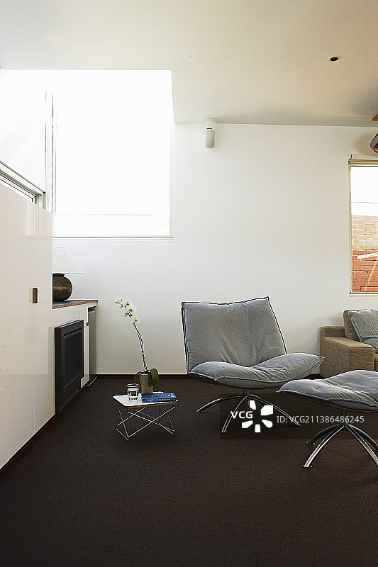 极简主义室内，深色地毯上的扶手椅和配套的脚凳图片素材