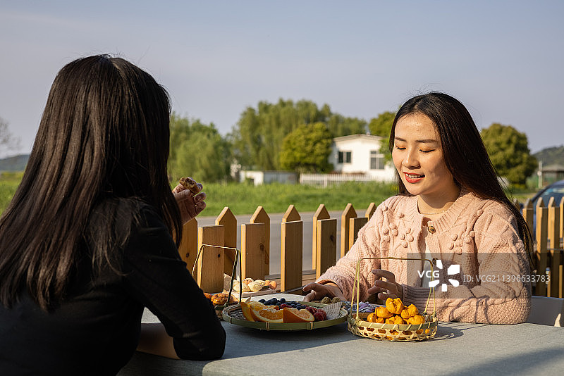 春季夕阳下两个年轻女孩社交聚会喝下午茶吃点心聊天图片素材