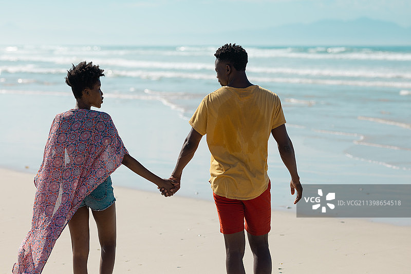 非洲裔美国年轻夫妇的后视图，牵手和走向大海对天空图片素材