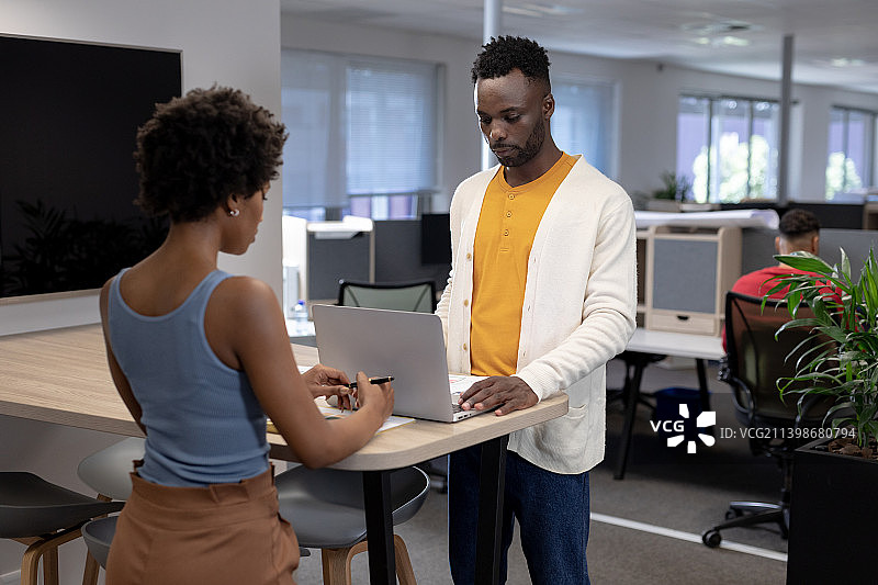 自信的非洲裔美国商人在办公室工作的女商人面前使用笔记本电脑图片素材