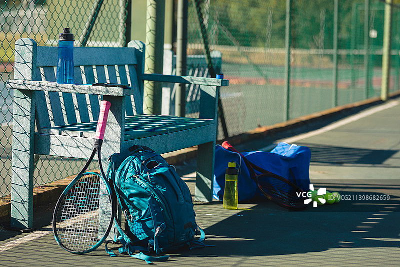 网球拍与背包和瓶子在球场的空木凳在阳光灿烂的日子图片素材