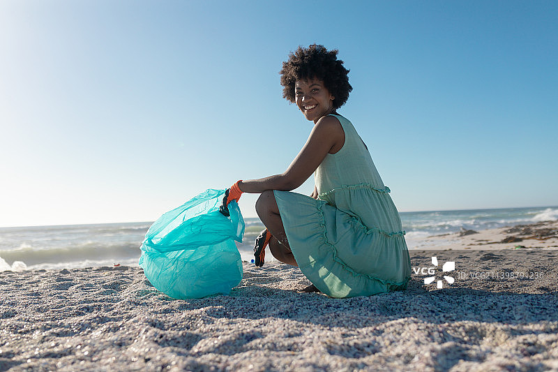 微笑的非洲裔美国人在收集垃圾时用塑料袋蹲着的侧视图肖像图片素材