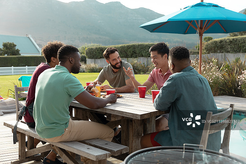 多种族的快乐男性朋友在夏天的时候坐在桌子旁喝酒聊天图片素材