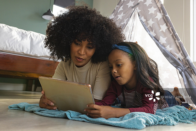 混血母亲带着女儿躺在家里的毛毯帐篷里用数码平板电脑看电影图片素材