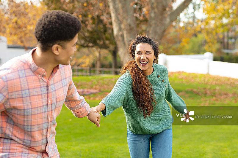 一对幸福的混血夫妇，手牵着手，微笑着在花园里散步图片素材