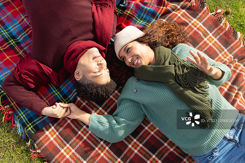 幸福的混血夫妇躺在地毯上，手牵着手，彼此微笑在秋天的花园图片素材