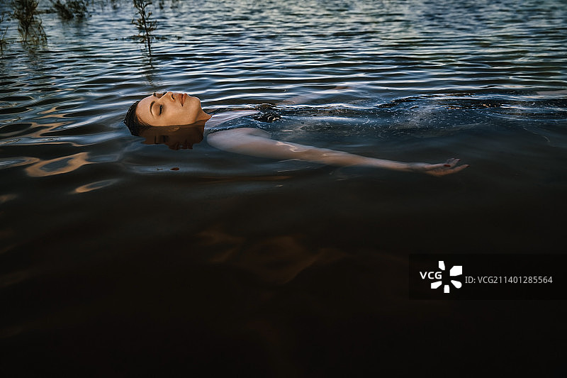 穿着衣服的女人浮在带着海草的池塘里。她看起来像淹死了。当她浮在水面上时，水溢出了她的身体。很适合做书封面图片素材