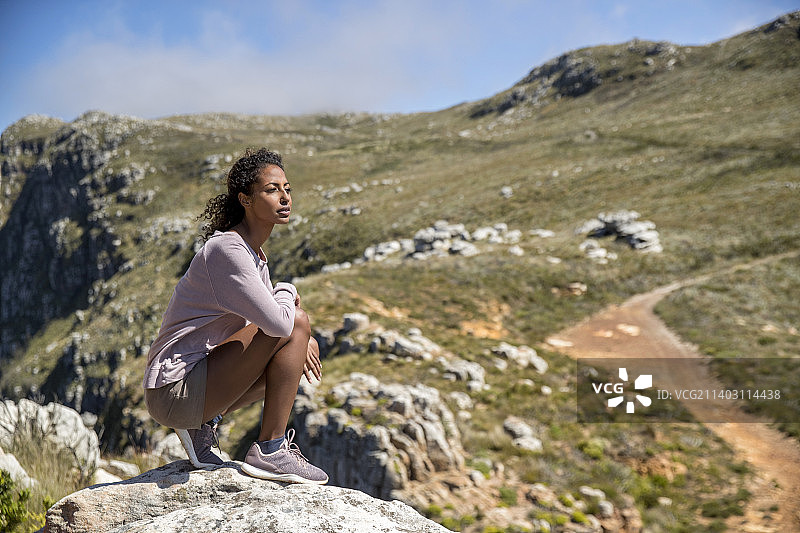 在山里徒步旅行时，年轻女子蹲在岩石上图片素材