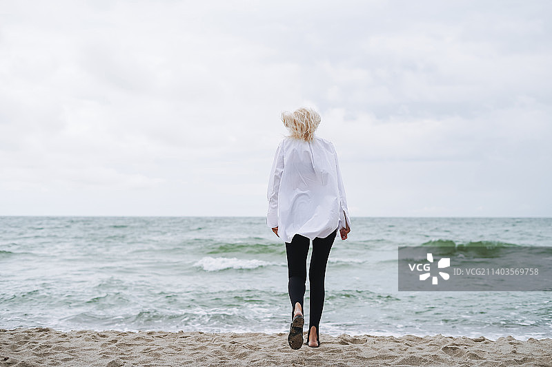 优雅的金发女人在白色衬衫上的沙滩在风暴海在大风天气图片素材