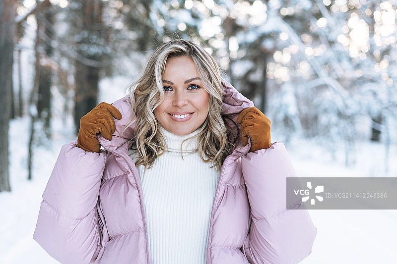 在俄罗斯斯维尔德洛夫斯克州叶卡捷琳堡皑皑白雪的冬季森林里，身穿冬装、金发碧眼的微笑金发女子的肖像图片素材