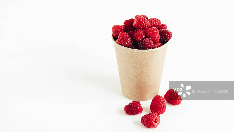 新鲜的红覆盆子放在纸杯里，白色的桌子背景图片素材