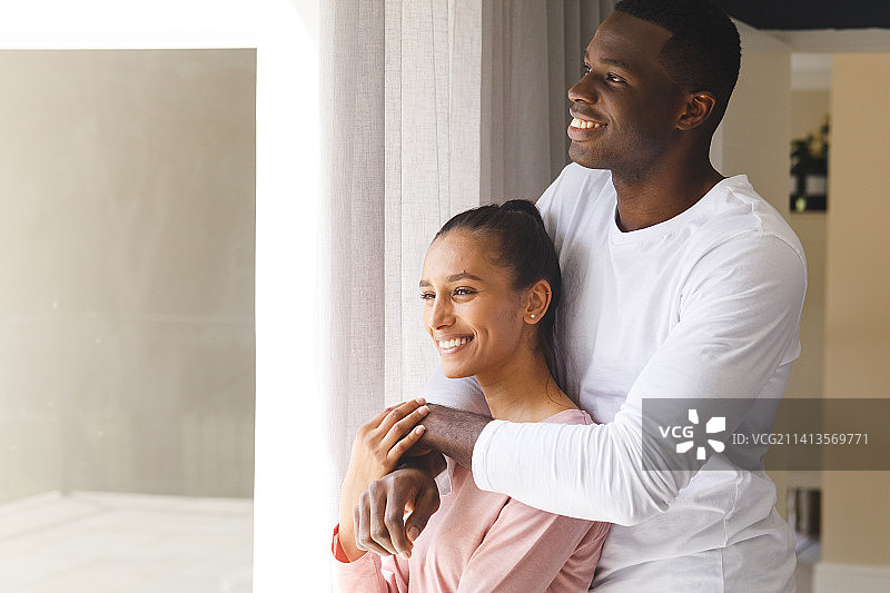 幸福的不同的夫妇拥抱，看着窗外，微笑在家里图片素材