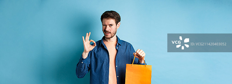 现代男子在休闲服装显示购物袋和好的标志图片素材