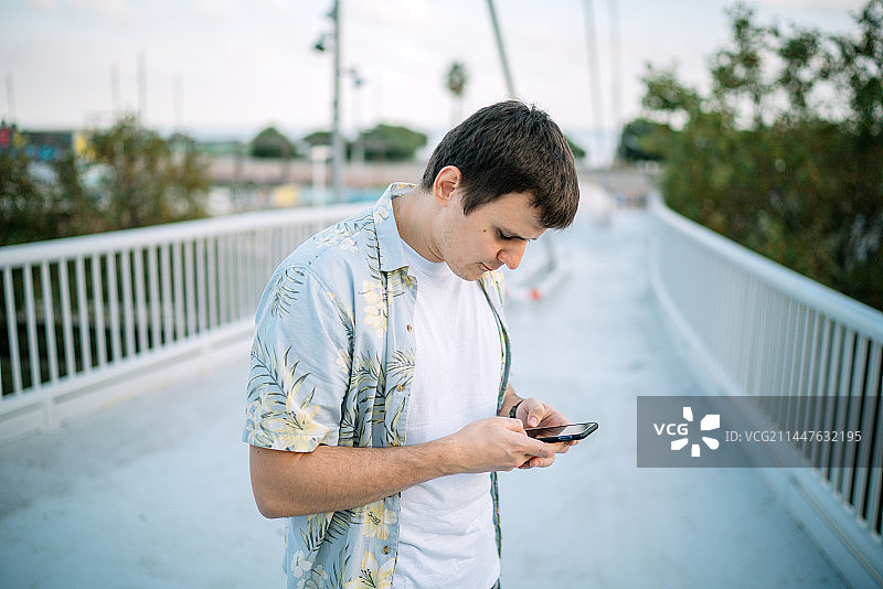 西班牙巴塞罗那，一个年轻人站在人行天桥上玩手机图片素材