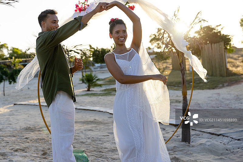 快乐的多元化新娘和新郎在他们的海滩婚礼上跳舞图片素材