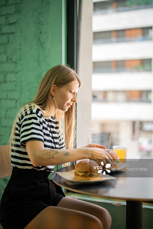 年轻女子在餐厅窗台边吃大汉堡的肖像图片素材