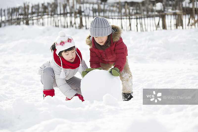 快乐的孩子们在雪地上滚雪球图片素材