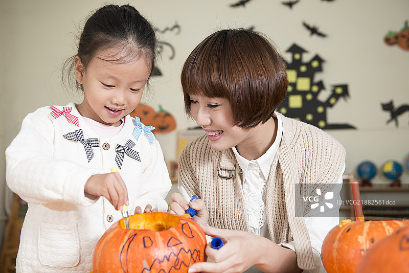 Kindergarten teacher and girl carving pumpkin图片素材